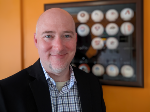 Simon Reilly standing in front of an orange wall and baseball display case.